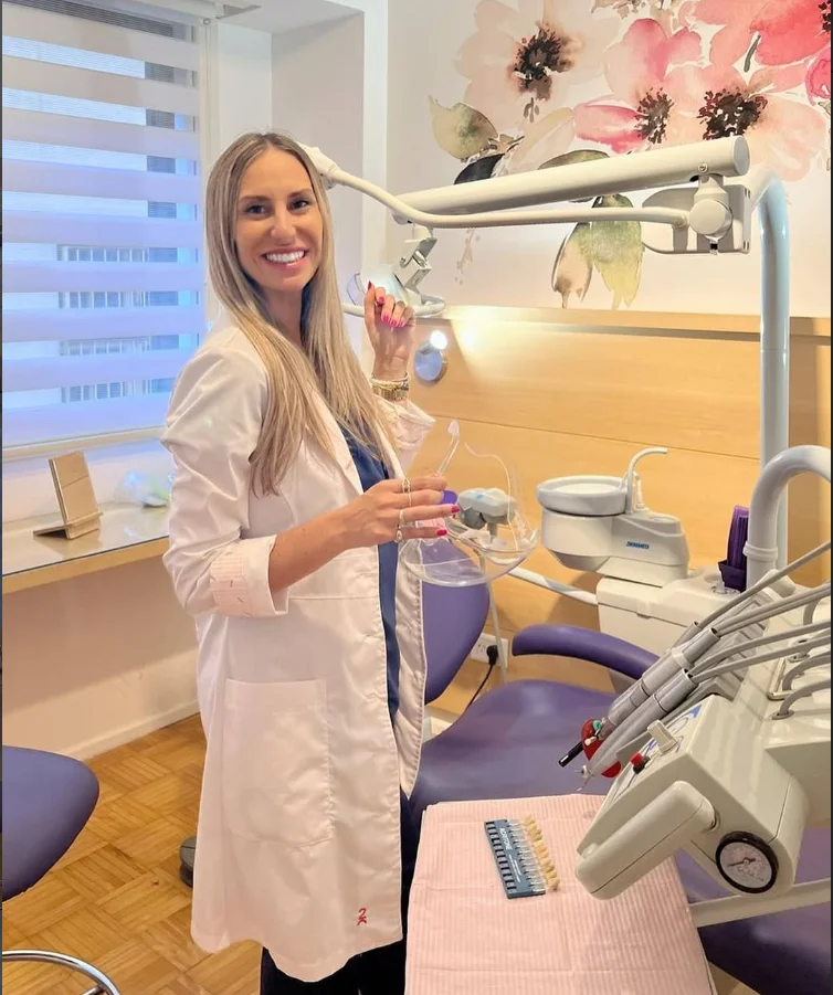 Dra. María Belén Livio en el box clínico con sillón violeta, mural de peonías y muestrario de tonos dentales